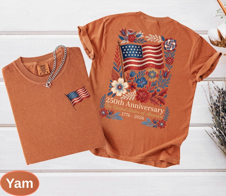 May include: Two yam-colored t-shirts. One has a small embroidered American flag on the chest. The other features a large American flag design on the back, surrounded by flowers, with the text "250th Anniversary The United States of America 1776-2026."