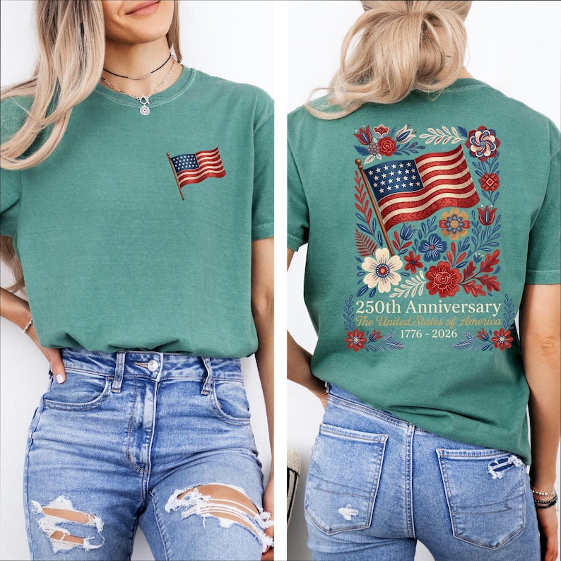 May include: Teal-colored t-shirt with an embroidered American flag on the front. The back features a larger flag design surrounded by flowers and the text "250th Anniversary The United States of America 1776-2026".