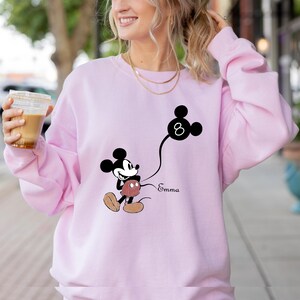 Puede incluir: Sudadera rosa con un gr&aacute;fico de Mickey Mouse en blanco y negro sosteniendo un globo con el n&uacute;mero 8. El texto "Emma" est&aacute; impreso debajo del gr&aacute;fico.