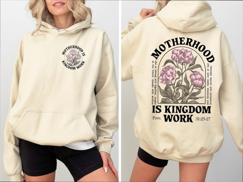 May include: Cream-colored hoodie with a front pocket and hood. The front features a circular design with the text "MOTHERHOOD IS KINGDOM WORK" and a floral illustration. The back has the same text and floral design, with additional text and scripture reference.