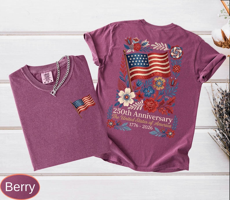 May include: Two berry-colored t-shirts. One has a small American flag patch, the other has a large American flag design with floral accents and text that reads "250th Anniversary The United States of America 1776-2026."