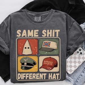 May include: Dark gray sweatshirt with the text "SAME SHIT DIFFERENT HAT" and four images of hats. The images include a white hood, a hat with a Confederate flag, a military hat, and a red baseball cap.