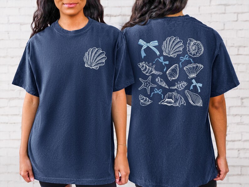 Puede incluir: Camiseta azul marino con un gr&aacute;fico de concha en la parte delantera y una colecci&oacute;n de conchas marinas, estrellas de mar y lazos en la parte trasera. El dise&ntilde;o es en blanco y azul claro. La camiseta est&aacute; hecha de un material suave y c&oacute;modo.