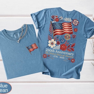 May include: Two blue jean t-shirts. One has a small embroidered American flag on the chest. The other has a large American flag design on the back, surrounded by flowers, with the text "250th Anniversary The United States of America 1776-2026."