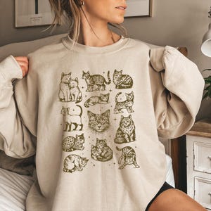 This sweatshirt shows multiple vintage cat illustrations in a 90s sketch style. The playful, cuddling, and sleeping kittens are surrounded by tiny stars for a magical look.