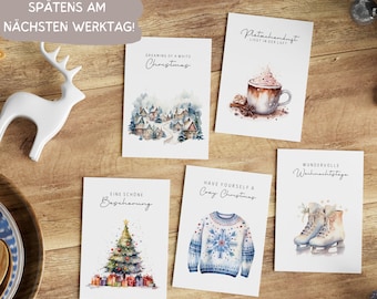 Könnte beinhalten: Fünf Weihnachtskarten mit Aquarell-Illustrationen. Die Karten zeigen ein verschneites Dorf, eine Tasse heiße Schokolade, einen Weihnachtsbaum, einen Pullover und ein Paar Schlittschuhe.