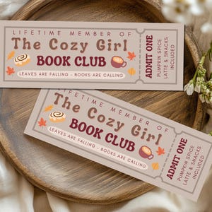 Könnte beinhalten: Zwei rechteckige Tickets mit dem Text "The Cozy Girl Book Club" und "Admit One" werden auf einem Holztablett angezeigt. Die Tickets zeigen herbstliche Illustrationen und den Satz "Leaves are falling - Books are calling."