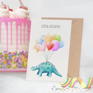 May include: A white card with the word "Einladung" printed in black. A blue dinosaur with a green back is holding onto colorful balloons, including hearts and stars. The card is sitting on a brown envelope.