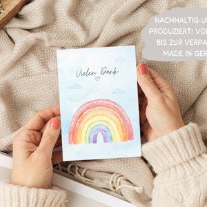 Op de afbeelding: Een lichtblauwe kaart met een regenboog en wolken. De kaart zegt "Vielen Dank" met een hartje. De kaart zegt ook "NACHHALTIG UND FAIR PRODUZIERT! VOM DESIGN BIS ZUR VERPACKUNG MADE IN GERMANY".