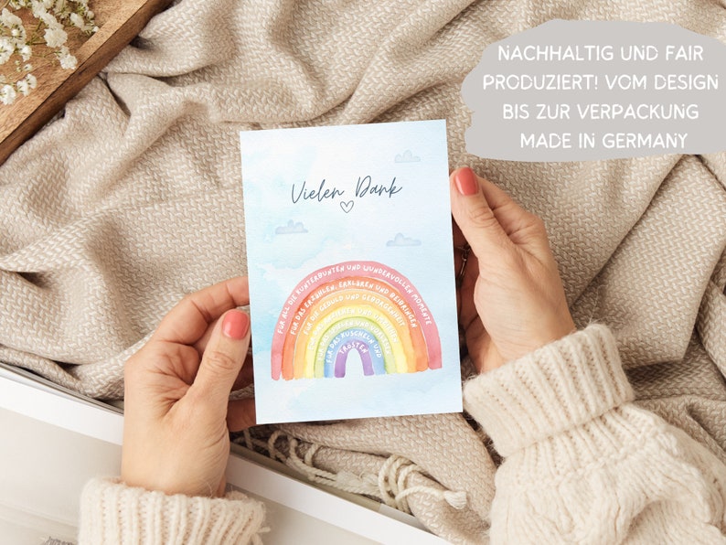 Op de afbeelding: Een lichtblauwe kaart met een regenboog en wolken. De kaart zegt "Vielen Dank" met een hartje. De kaart zegt ook "NACHHALTIG UND FAIR PRODUZIERT! VOM DESIGN BIS ZUR VERPACKUNG MADE IN GERMANY".