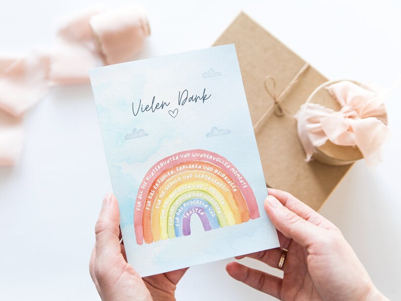 Op de afbeelding: Een kaart met een aquarel regenboog en de tekst "Vielen Dank" (Duits voor "Bedankt") met een hartje. De regenboog heeft tekst op elke band, waaronder "Voor alle kleurrijke en prachtige momenten", "Voor het vertellen, uitleggen en leren", "Voor het geduld en de veiligheid", "Voor het ruisen", "Voor het knuffelen", "Voor de troost en het vertrouwen".
