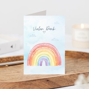 Op de afbeelding: Een kaart met een regenboogontwerp en de tekst "Vielen Dank" (Duits voor "Bedankt") met een hartje. De regenboog heeft tekst op elke band, waaronder "Voor al het plezier", "Voor het lachen", "Voor de herinneringen", "Voor het geduld", "Voor de liefde", "Voor de steun", "Voor de vriendelijkheid", "Voor de knuffels", "Voor de glimlachen", "Voor de vreugde", "Voor de magie", "Voor het wonder", "Voor de momenten".