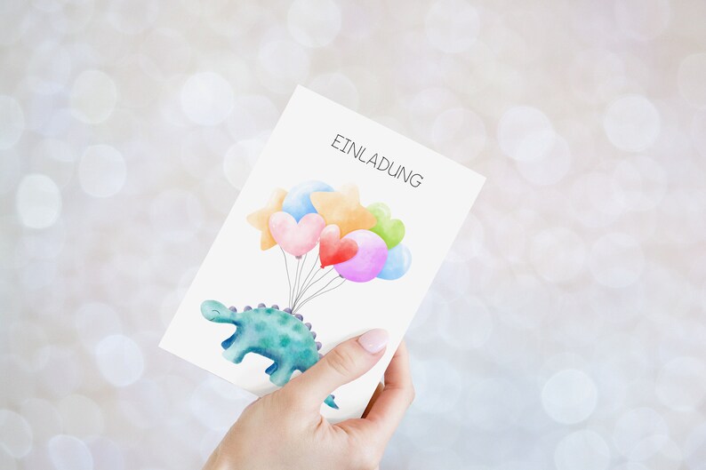 May include: A white card with the word "Einladung" printed on it. A green dinosaur with a blue belly is holding a string of colorful balloons, including hearts and stars.