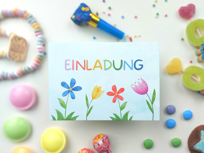 May include: A blue and white card with the word "EINLADUNG" in rainbow letters. The card has a watercolor background with three flowers: a blue flower, a yellow flower, and a red flower.