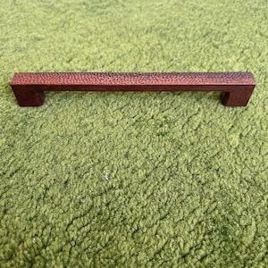 May include: A dark brown wooden cabinet pull with a textured surface.