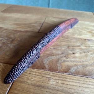 May include: A wooden handle with a textured, dark brown surface and a smooth, reddish-brown surface. The handle is curved and has a pointed end.
