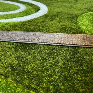 May include: A close-up of a wooden rectangular sign with a rough, textured surface. The sign is lying on a green, fuzzy surface.