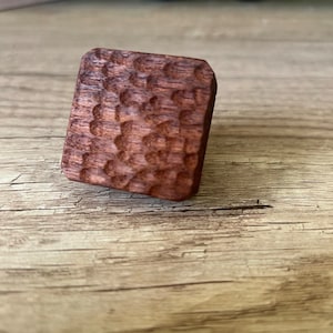 May include: A dark brown wooden ring with a textured surface. The ring is made of wood and has a unique design.