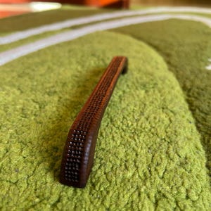 May include: A brown wooden cabinet door handle with a textured surface.