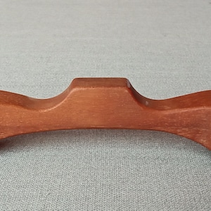 Puede incluir: Una manija de madera marrón arqueada con una superficie lisa y redondeada. La manija tiene un diseño único y curvo, ideal para muebles o armarios.