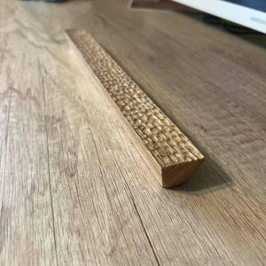 May include: A wooden decorative trim with a textured surface. The trim is light brown in color and has a rounded edge.