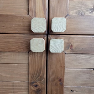 Puede incluir: Dos puertas de armario de madera con cuatro pomos cuadrados de madera. Las puertas son de color marrón oscuro y los pomos son de color marrón claro.