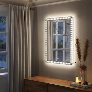 May include: A rectangular mirror with a white light border. The mirror is mounted on a wall above a wooden dresser.