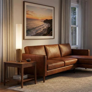 May include: A living room scene featuring a brown leather sectional sofa, a wooden side table, and a tall, cylindrical floor lamp. A framed landscape art piece hangs on the wall. The room has neutral-toned curtains and a patterned rug.