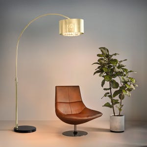 May include: A gold arc floor lamp with a scalloped lampshade illuminates a brown leather swivel chair and a potted plant. The lamp has a black circular base. The chair is on a silver base. The plant is in a gray concrete pot.