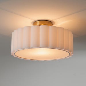 May include: A white, scalloped-edge ceiling light fixture with a brass-colored base. The light has a cylindrical shade with vertical pleats. The light is turned on, illuminating the room with a soft glow. Home decor.