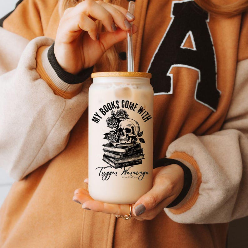 may include; a frosted glass with a bamboo lid that has a black graphic of a stack of books with a skull resting on top. There are also roses included in the design by the skull. The text on the design reads 'my books come with trigger warnings'