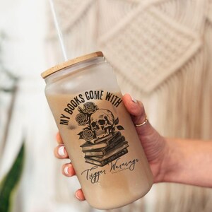 may include; a frosted glass with a bamboo lid that has a black graphic of a stack of books with a skull resting on top. There are also roses included in the design by the skull. The text on the design reads 'my books come with trigger warnings'