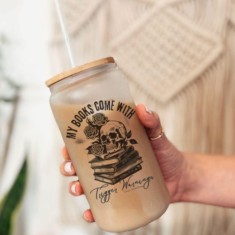 may include; a frosted glass with a bamboo lid that has a black graphic of a stack of books with a skull resting on top. There are also roses included in the design by the skull. The text on the design reads 'my books come with trigger warnings'