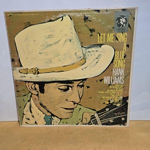 May include: Album cover for "Let Me Sing a Blue Song" by Hank Williams. The artwork features a painted portrait of a man wearing a cowboy hat and playing a guitar. The album title and artist's name are in bold text.
