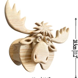 May include: A wooden moose head sculpture, featuring detailed carving and a natural wood finish. The sculpture measures 13.8 inches wide and 11.2 inches high. The moose has large antlers and a whimsical expression.