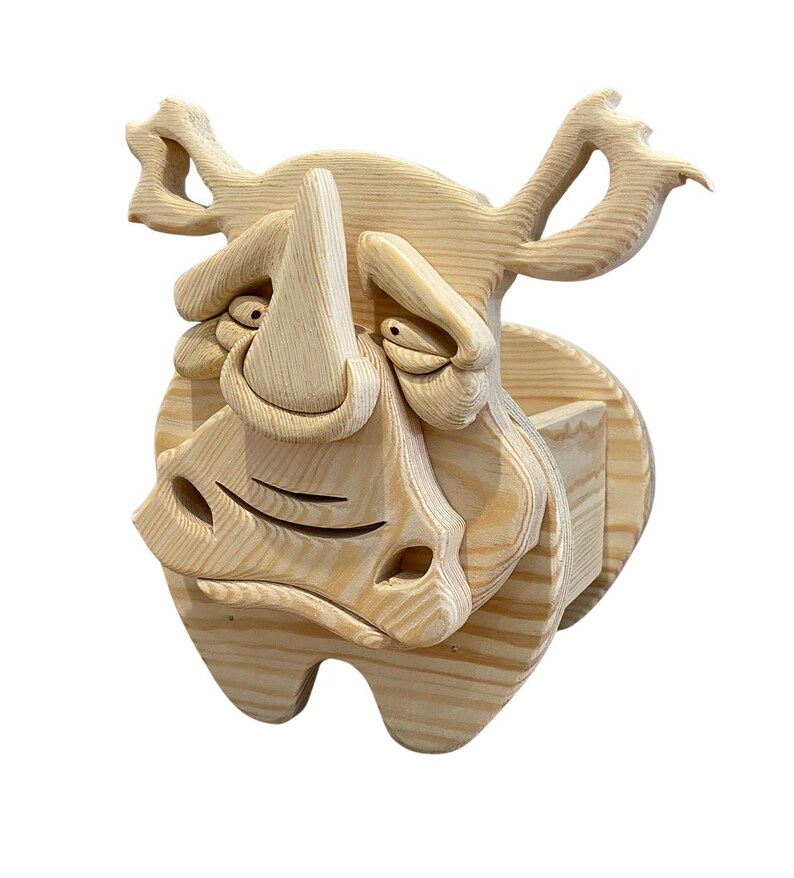 May include: A whimsical wooden rhino sculpture with a cartoonish design. The rhino is carved from light-colored wood, featuring exaggerated facial features, including a large horn, expressive eyes, and a wide, smiling mouth. The sculpture is mounted on a circular wooden base.