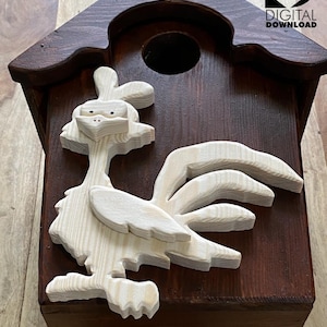 Pode incluir: Uma casa de pássaros de madeira pintada de marrom com um pássaro de madeira clara recortado na frente. O pássaro é um beija-flor estilizado com uma cauda longa e um bico.