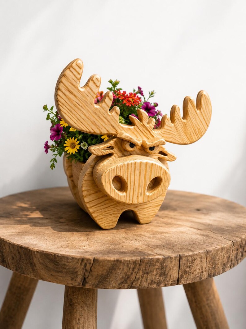 K&ouml;nnte beinhalten: Ein h&ouml;lzerner Elch-Blumentopf gef&uuml;llt mit bunten Blumen. Der Elch hat gro&szlig;e Geweihe und ein detailliertes Gesicht. Der Pflanztopf steht auf einem rustikalen Holzschemel und schafft eine charmante, nat&uuml;rliche &Auml;sthetik. Die Blumen umfassen gelbe, rote und violette Bl&uuml;ten.