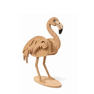 May include: A wooden flamingo sculpture with a natural wood finish. The bird has a long neck, a black beak, and detailed wing and tail feathers. It stands on an oval base, showcasing a handcrafted design.