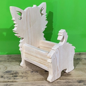 May include: A wooden decorative planter shaped like a dog. The planter is made of light-colored wood and features a dog-like silhouette with cut-out details for the ears and tail. The planter is designed to hold small plants or decorative items.