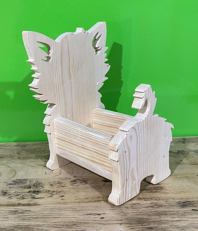 May include: A wooden decorative planter shaped like a dog. The planter is made of light-colored wood and features a dog-like silhouette with cut-out details for the ears and tail. The planter is designed to hold small plants or decorative items.