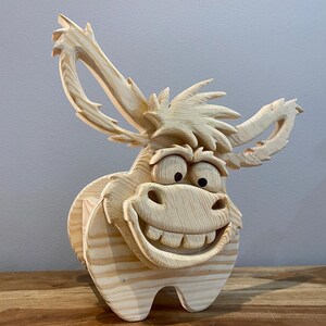 May include: A whimsical, wooden donkey sculpture with a large, smiling face and oversized ears. The donkey is carved from light-colored wood, showcasing the natural grain. The sculpture has a cartoonish design, perfect for home decor.