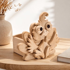 May include: A wooden box with a carved rooster design. The rooster has large eyes, a beak, and detailed feathers. The box is made of light-colored wood and sits on a wooden table. A vase with dried plants is in the background.