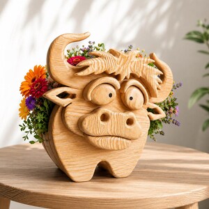 May include: A whimsical wooden bull planter filled with colorful flowers. The handcrafted planter features a cartoonish bull face with large eyes, horns, and a textured mane. The planter is filled with vibrant orange, red, purple, and yellow flowers, creating a cheerful display.