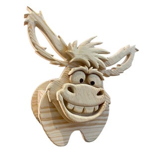 May include: A wooden donkey head sculpture with a large, toothy grin and expressive eyes. The donkey has large, upright ears and a textured mane. The sculpture is made of light-colored wood and is likely intended for wall mounting.