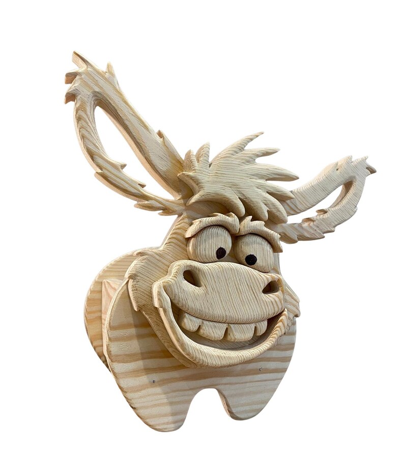 May include: A wooden donkey head sculpture with a large, toothy grin and expressive eyes. The donkey has large, upright ears and a textured mane. The sculpture is made of light-colored wood and is likely intended for wall mounting.