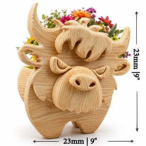 K&ouml;nnte beinhalten: Ein Holz-Pflanzgef&auml;&szlig; in Form einer Highland-Kuh, 23 cm hoch und 23 cm breit, gef&uuml;llt mit bunten Blumen. Der Pflanztopf ist aus hellem Holz geschnitzt und weist detaillierte Gesichtsz&uuml;ge und H&ouml;rner auf. Die Kuh hat ein skurriles, cartoonartiges Design.