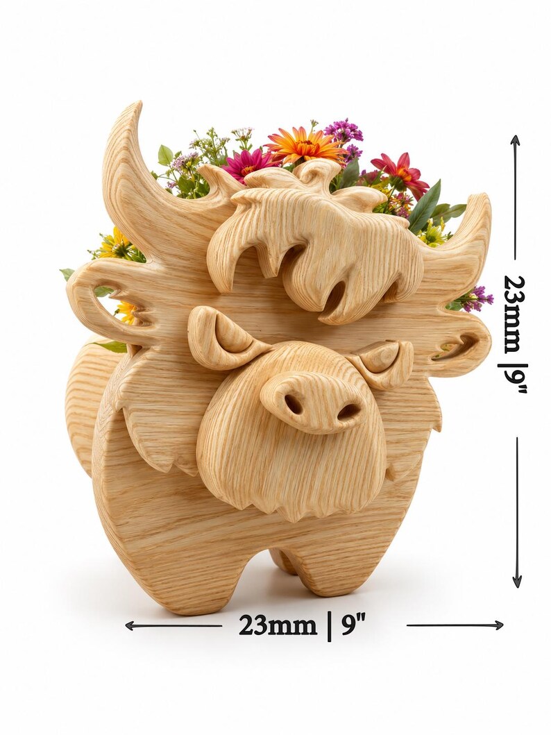 K&ouml;nnte beinhalten: Ein Holz-Pflanzgef&auml;&szlig; in Form einer Highland-Kuh, 23 cm hoch und 23 cm breit, gef&uuml;llt mit bunten Blumen. Der Pflanztopf ist aus hellem Holz geschnitzt und weist detaillierte Gesichtsz&uuml;ge und H&ouml;rner auf. Die Kuh hat ein skurriles, cartoonartiges Design.