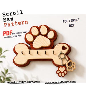 May include: A wooden wall-mounted key holder shaped like a dog bone with a paw print design on top. The piece features a dark stained base with a light wood overlay, five black metal hooks, and two dangling paw-shaped keychains. Text reads Scroll Saw Pattern, PDF/SVG/DXF, PDF for scroll saw - pages ready to print, and woodart513jm.etsy.com.