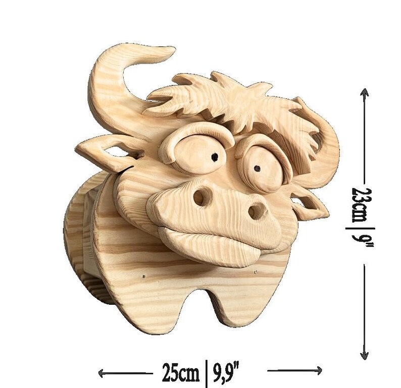 May include: A wooden bull head sculpture, measuring 9 inches high and 9.9 inches wide. The sculpture is made of light-colored wood and features a cartoonish design with large eyes and a prominent snout. The bull has a whimsical, friendly appearance.